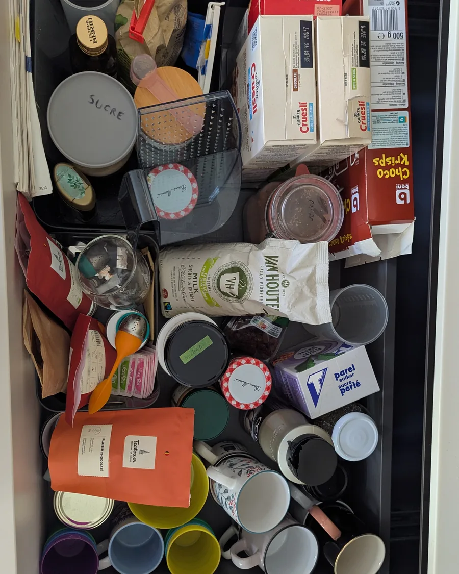 Tiroir de cuisine avant rangement, vu du dessus : céréales, sachets, tasses et boîtes en vrac